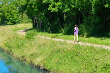 Active woman runner jogging near canal river, outdoors running, sport and healthy lifestyle concept
