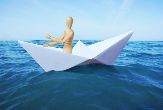Man sails on the sea in a toy paper ship. Abstract image with a wooden puppet