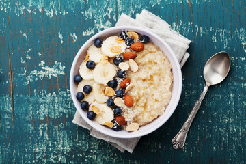 Bowl of oatmeal porridge with banana, blueberries, almonds, coconut and caramel sauce on teal...