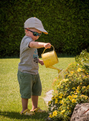 Kleiner Junge mit Giesskanne wässert Blumen im Sommer