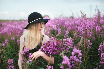 beautiful girl in black dress and hat standing in a field of lupine flowers