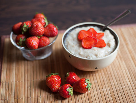 hot oatmeal, with pieces of strawberries and warm cocoa with milk on a wooden table