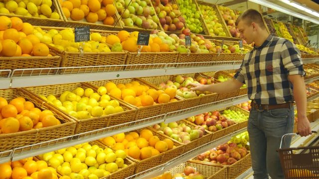 Man Selecting Fresh Red Apples In Grocery Store Produce Department And Smelling It. Young Handsome Guy With Shop Basket Is Choosing Apples In Supermarket.