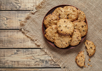 Homemade baked cereal oatmeal cookies with raisins and chocolate healthy sweet dessert snack food on vintage cloth on wooden table background.