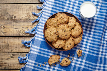 Traditional baked cereal oatmeal cookies with raisins and chocolate healthy sweet dessert snack food with glass of milk on clay dish on wooden table background.