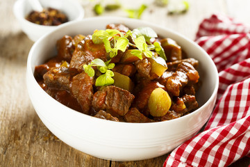 Goulash, served in white bowl with fresh herbs