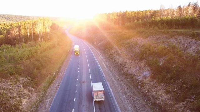Flights above highway road at the sunset. Aerial view of trucks on the road.