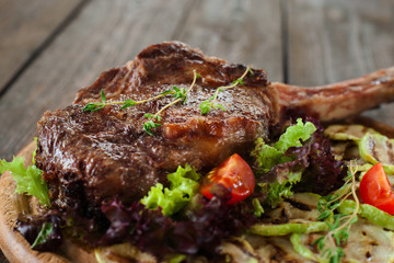 Grilled ribeye steak on bone with vegetable marrow, lettuce and tomatoes on wooden background