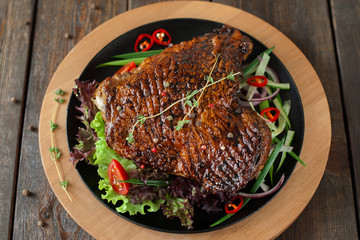 Top view on baked chicken duck with herbs on black plate on wooden background, flat lay