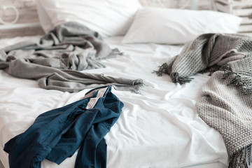 Wrinkled shirt lying on unmade bed closeup. Blue shirt lie about messy bed on wrinkled sheet near...
