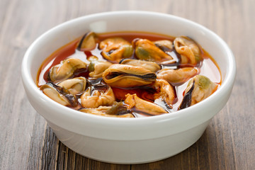 mussels in sauce in white bowl on brown wooden background