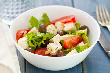salad cheese with vegetables in white bowl on blue background
