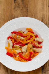 chicken with red pepper and carrot on white plate on brown wooden background