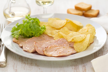 fried meat with potato chips and fresh lettuce on white dish on white wooden background