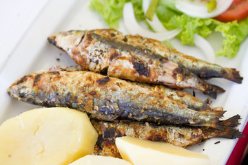 grilled sardines with potato and salad on white dish