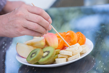 closeup of a hand that stings delicious fresh cut fruit on a plate