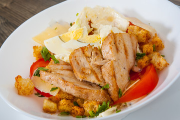 Caesar salad with croutons, cheese, eggs, tomatoes and grilled chicken on wooden table