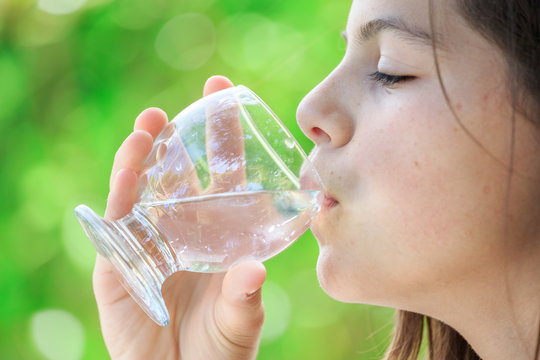 closeup of a healthy young girl drinking glass of water outdoors