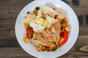 Caesar salad with croutons, cheese, eggs, tomatoes and grilled chicken on wooden table