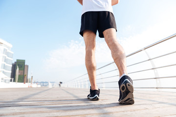 Legs of young man in black sneakers running on pier