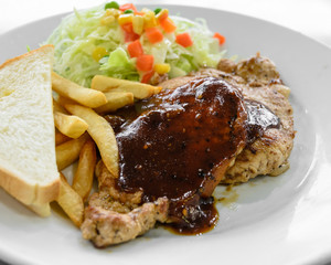 Grilled pork steak fillet with salad and French fries on white plate