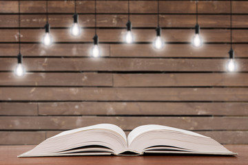 Vintage open book on the desk and light bulbs on the background