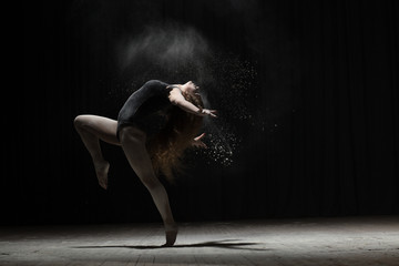 Flexible woman dancing with flour on black background