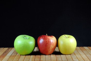 Three apples on teakwood shelf and black background.
