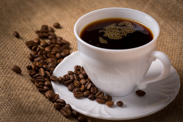 Tasse Kaffee mit Untertasse und Kaffeebohnen auf Leinentuch, Nah