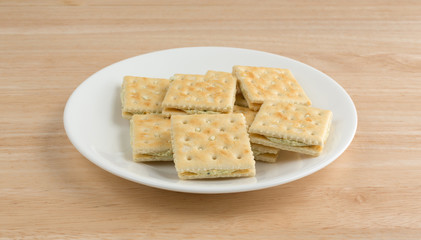 Cream cheese and chives crackers on a white plate atop a wood table.