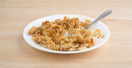 Chicken in a sauce with rice and veggies on a plate atop a wood table.