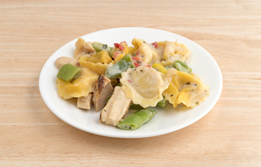 Chicken and tortellini TV dinner on a white plate atop a wood table.
