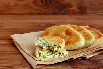 Fried pies with homemade cottage cheese, green onion and dill on paper and wooden background. Yeast-free pies recipe. A rustic style. Close-up