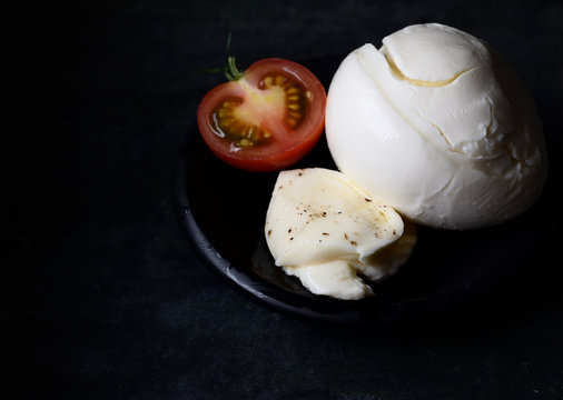 Delicious cheese mozzarella, tomatoes and basil leaves in black bowl and dark background