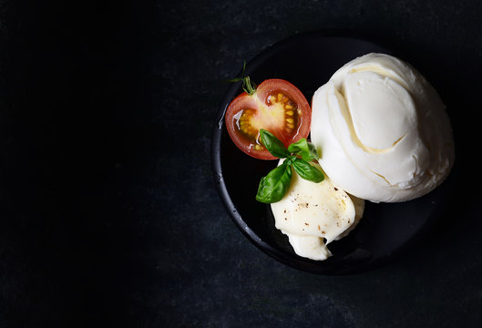 Delicious cheese mozzarella, tomatoes and basil leaves in black bowl and dark background