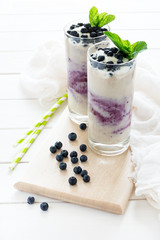 Two glasses with fresh blueberry smoothie decorated berries and mint leaves on white wooden background. Selective focus