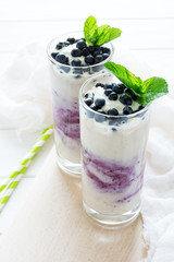 Two glasses with fresh blueberry smoothie decorated berries and mint leaves on white wooden background. Selective focus