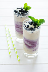 Two glasses with fresh blueberry smoothie decorated berries and mint leaves on white wooden background. Selective focus