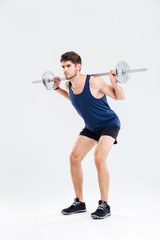 Attractive young sportsman holding barbell and doing squats