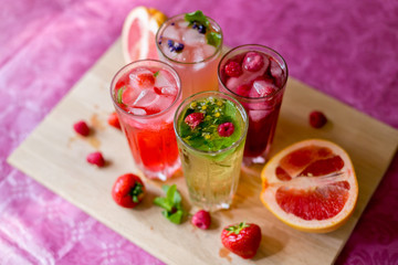 Four homemade refreshing summer cocktails and drinks with ice fresh berries, strawberry, raspberry and grapefruit on wooden cutting Board top view