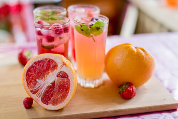 Four homemade refreshing summer cocktails and drinks with ice fresh berries, strawberry, raspberry and grapefruit on wooden cutting Board  