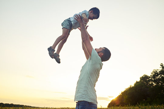 Happy father lifting his small son on background of sunset sky