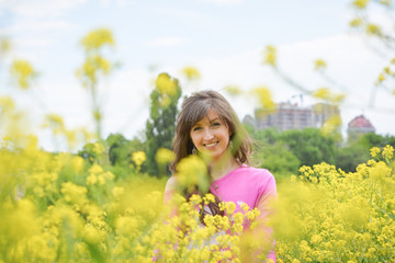 Naklejka na ściany i meble A beautiful young woman on a field. Stylish brunette girl standing in the yellow flower field on a sunny day in summer. Concept of freedom and happiness 