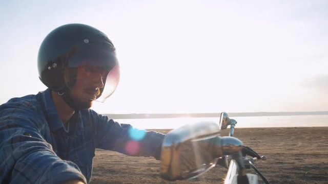 Motorcyclist sitting on his motorbike on the road near the sea during sunset