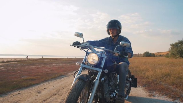Motorcyclist driving his motorbike on the road during sunset near the water