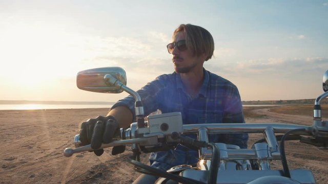 Motorcyclist sitting on his motorbike on the road near the sea during sunset