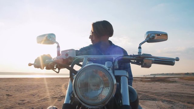 Motorcyclist sitting on his motorbike on the road near the sea during sunset
