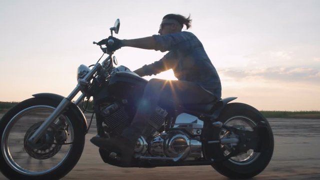 Motorcyclist driving his motorbike on the road during sunset near the water