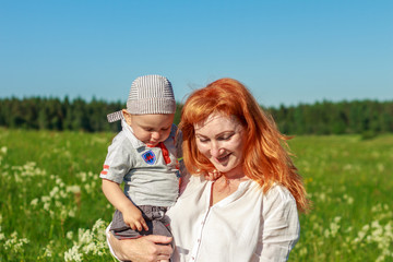 Beautiful red-haired mother playing with her baby in the field.