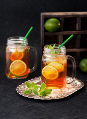 Cold tea with lime and mint in glass jars on black grunge background